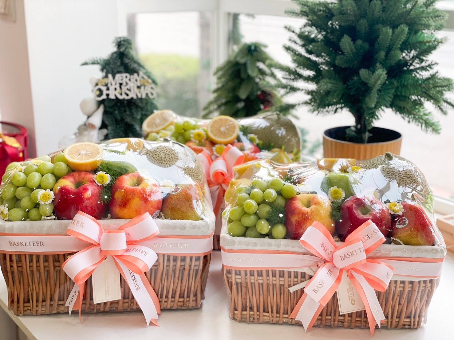 Fresh fruit gift basket with grapes, apples, pears, and cantaloupe, wrapped in a wicker basket and adorned with a peach ribbon.