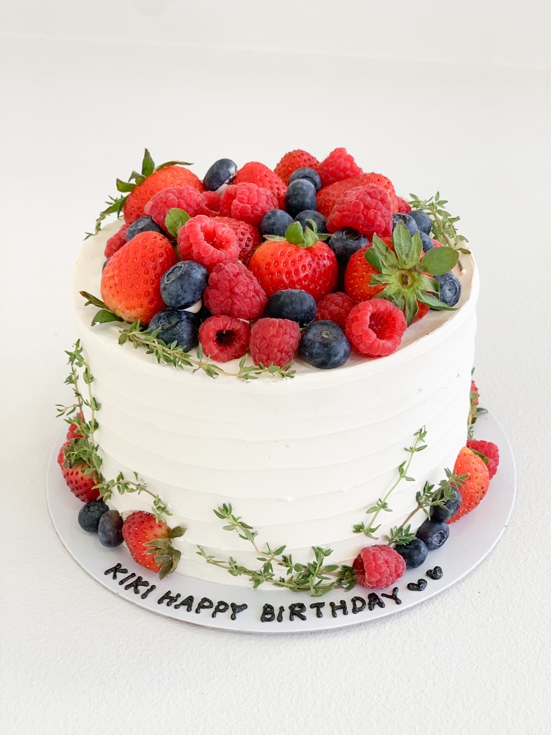 White vanilla birthday cake topped with strawberries, blueberries, raspberries, and fresh thyme.