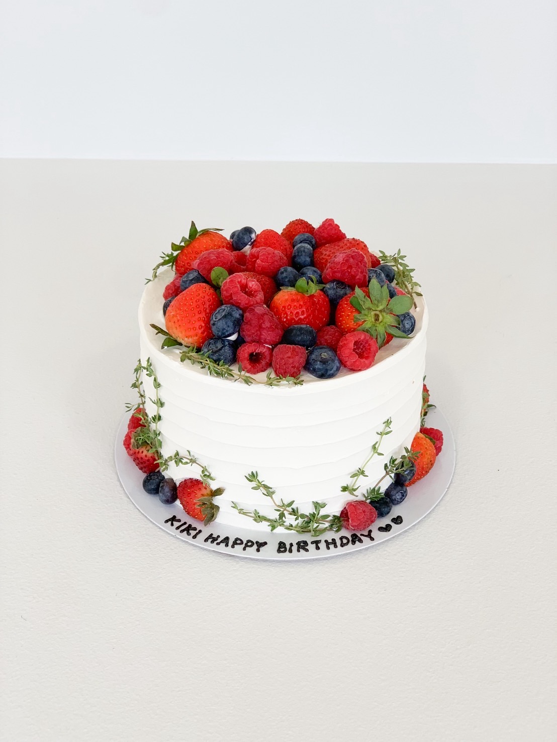 White vanilla birthday cake topped with strawberries, blueberries, raspberries, and fresh thyme.