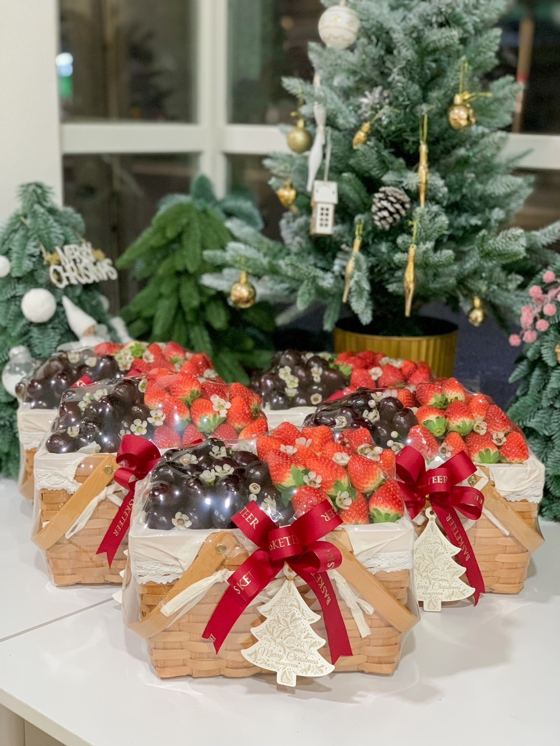 Holiday fruit basket filled with fresh strawberries and grapes, wrapped with red ribbons, lace, and a Christmas tree tag.