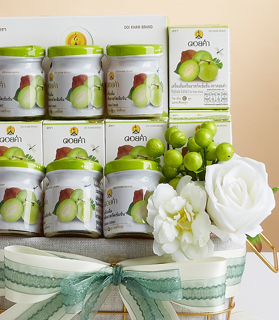 A luxurious display featuring Doi Kham brand products, elegantly presented in a sophisticated woven basket. The ensemble includes jars and boxes showcasing images of luscious green fruits on their labels, evoking a sense of freshness and quality. The arrangement is beautifully accented with pristine white roses and vibrant green berries, nestled amongst decorative green and white ribbons bearing the prestigious Basketeer logo.