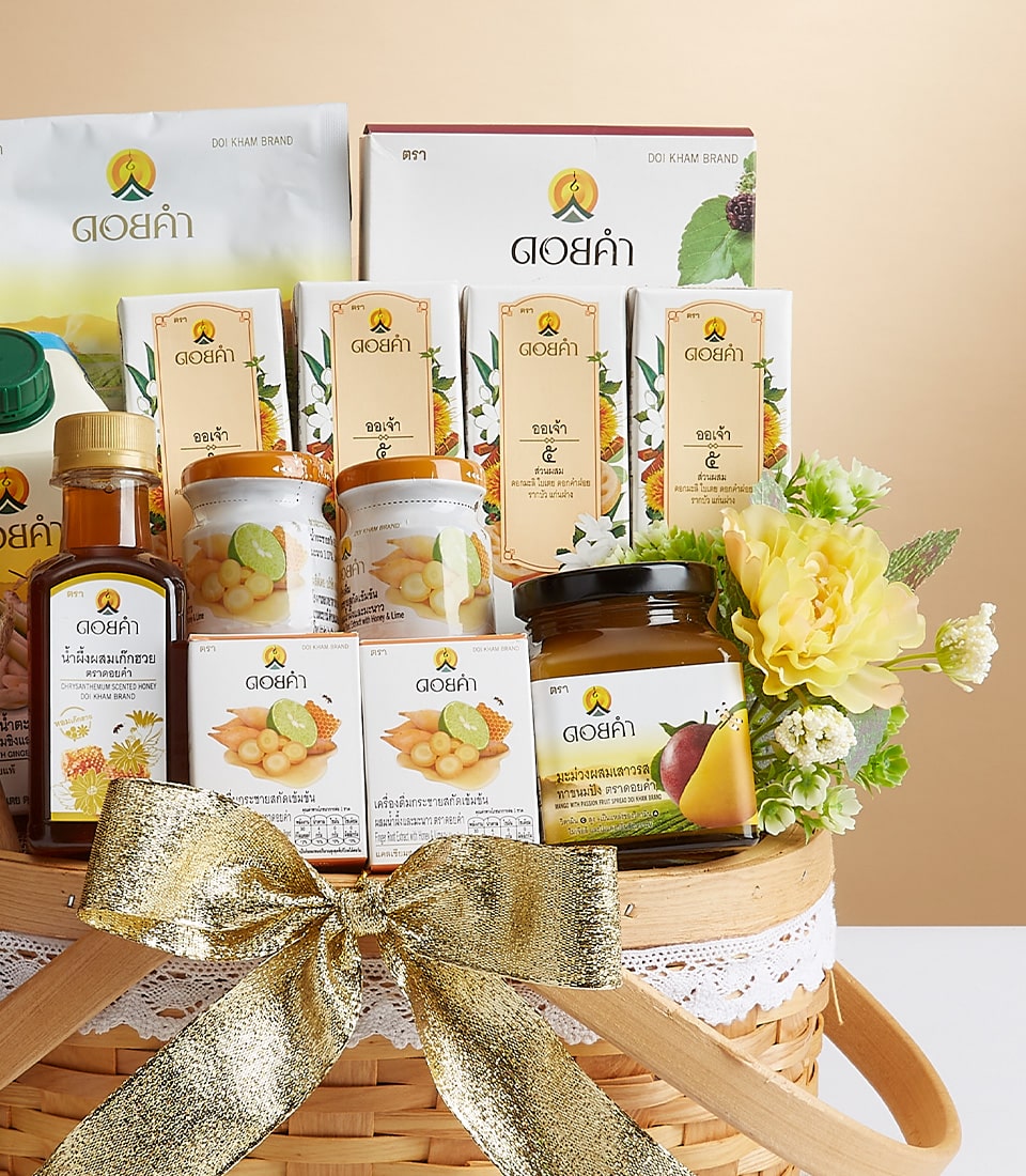 A lavishly adorned wicker basket, graced with an elegant gold ribbon and the distinguished Basketeer logo, showcases a curated selection of Doi Kham's premium offerings. This exquisite assortment features an array of fruit juices, delightful jams, herbal supplements, gourmet snacks, and luxurious tea boxes. The arrangement is further elevated by the charming addition of vibrant yellow flowers and lush greenery, creating an inviting display that epitomizes luxury and refinement.