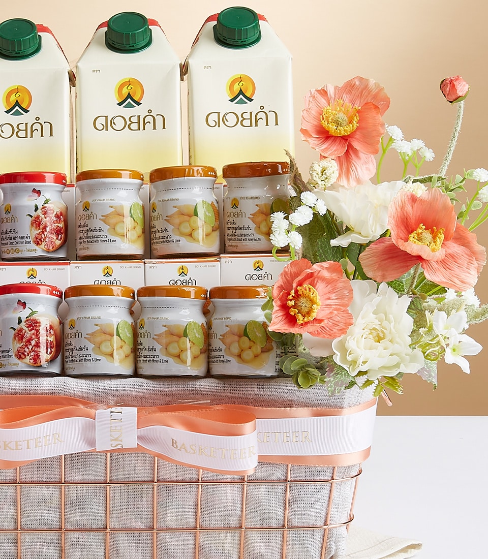 A luxurious gift basket brimming with a selection of premium juice cartons and cans, artfully arranged among orange, white, and peach blossoms. The opulent ensemble is elegantly adorned with a sophisticated white and gold ribbon featuring the distinctive 