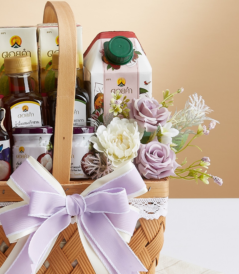 A luxurious wicker basket curated by Basketeer, elegantly filled with an exquisite selection of premium cartons of juice, and bottled beverages. This sophisticated gift is further enhanced with delicate artificial flowers in pristine white and enchanting lavender hues. The basket is adorned with a refined white lace trim and a stunning purple and white ribbon bow, proudly displaying the Basketeer logo for an extra touch of opulence.