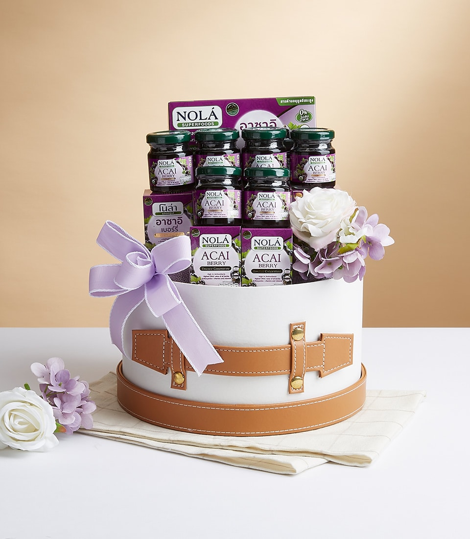 A sophisticated white and brown gift basket luxurious adorned with a large lavender ribbon and accentuated with elegant white and lavender flowers. Nestled inside are several exquisite jars of NOLA Acai Berry Extract, promising a taste of opulence. The elegant presentation is completed by the presence of the esteemed Basketeer logo on the ribbon. The serene beige gradient backdrop enhances the inviting allure of this remarkable gift.