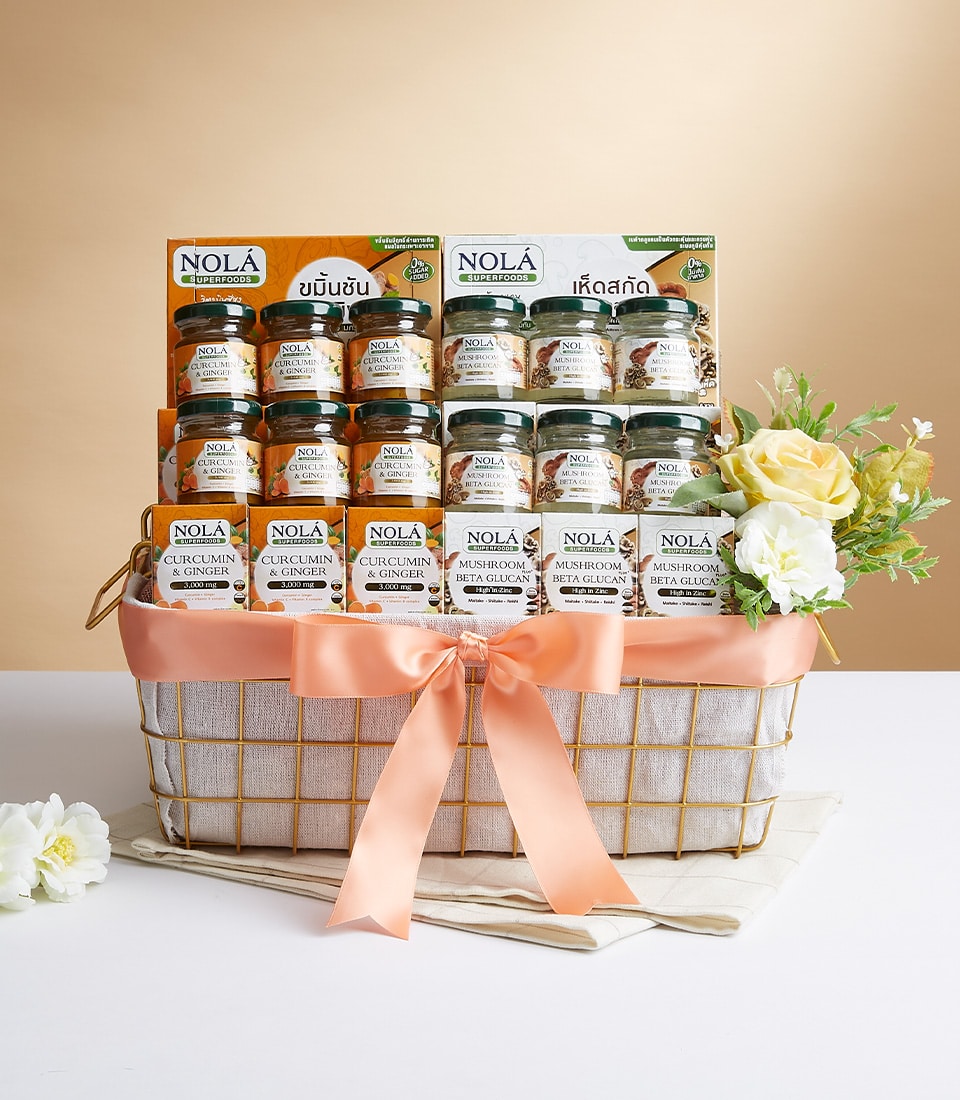 A luxurious woven basket brimming with an exquisite selection of Nola's curated delights, featuring jars of curcumin ginger and mushroom beverages. This enchanting ensemble is gracefully adorned with a sophisticated peach ribbon bearing the distinguished Basketeer logo, complemented by an arrangement of elegant yellow and white flowers. The entire scene is set against a light beige gradient backdrop, exuding an inviting warmth and opulence.