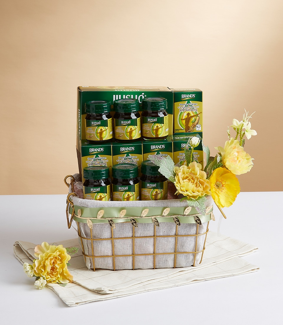 A beautifully woven wicker basket brimming with six elegant jars of Brand's Bird's Nest drink, adorned with vibrant yellow blooms and lush green foliage. Behind this luxurious arrangement stands an exquisite boxed set of the same premium product, proudly showcasing the Basketeer logo. The entire scene is artfully presented on a pristine white cloth against a serene neutral backdrop, evoking a sense of opulence and sophistication.
