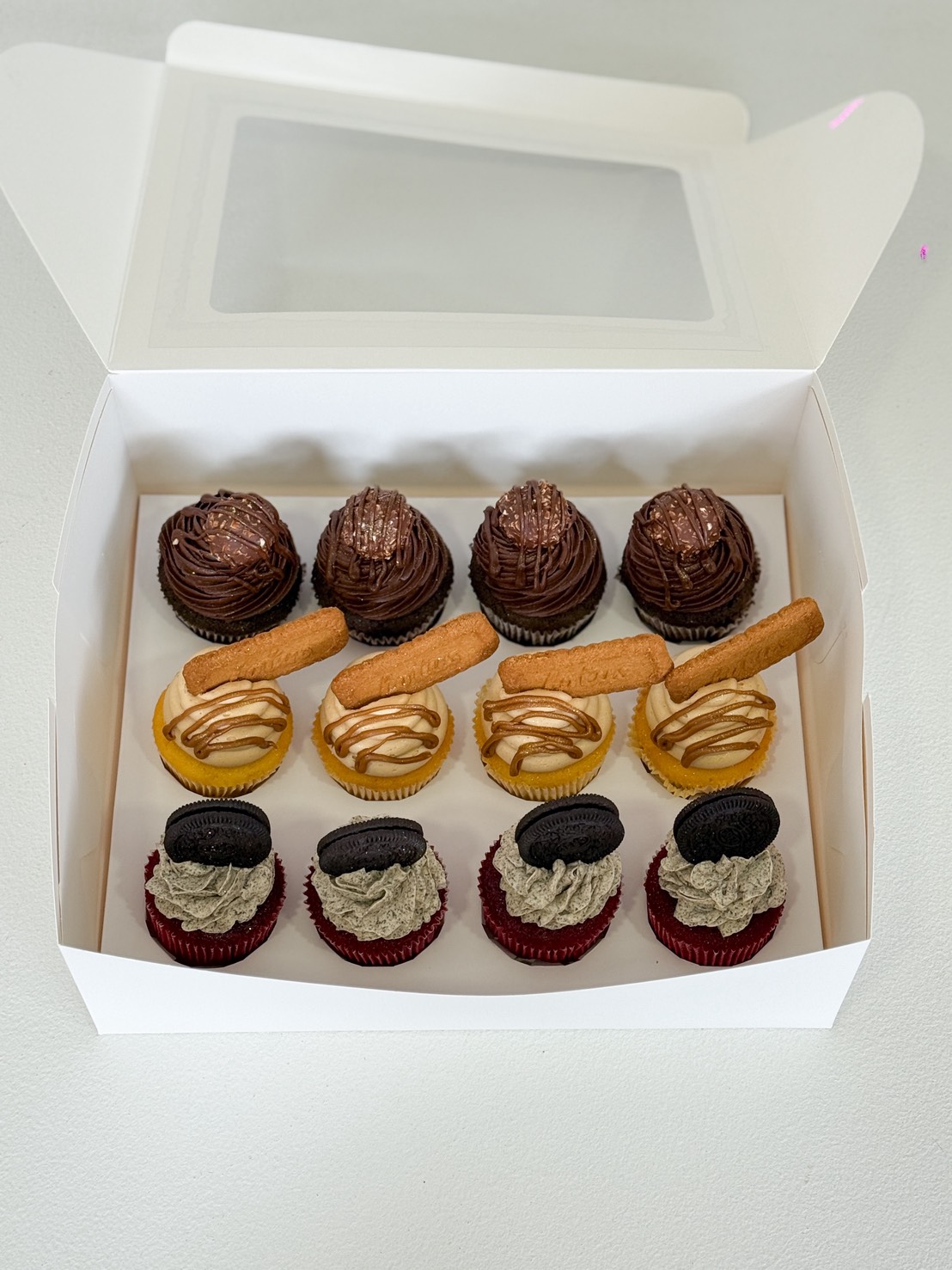 A white box featuring a Mix and Match Chocolate Selection: nine assorted cupcakes, including chocolate cupcakes with swirled icing, cupcakes with yellow filling and biscuit sticks, and red velvet cupcakes topped with cookies and cream.