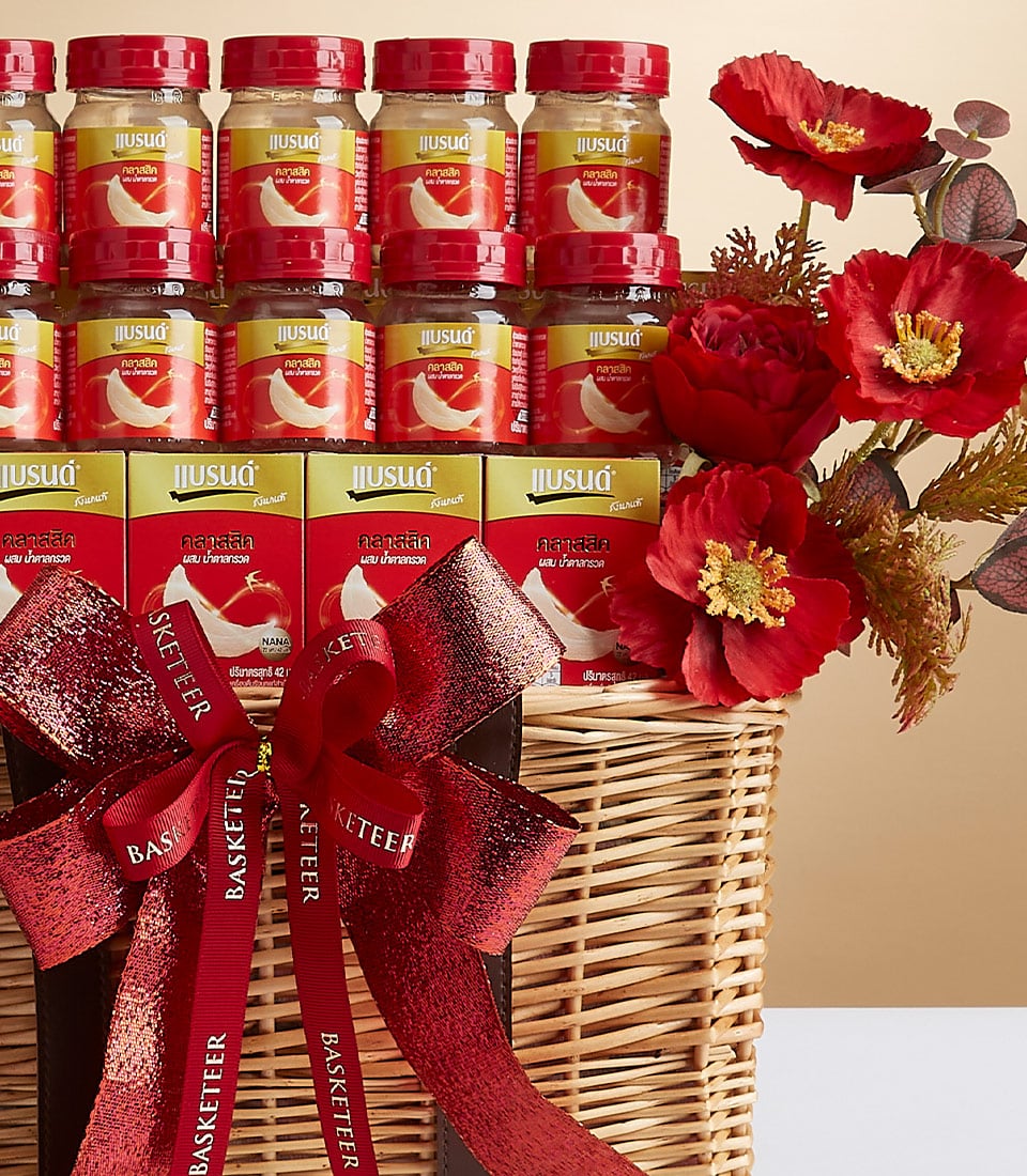 A luxurious wicker gift basket graced with an elegant red and black ribbon bow, showcasing the prestigious Basketeer logo. This opulent arrangement features multiple jars of the premium health supplement 