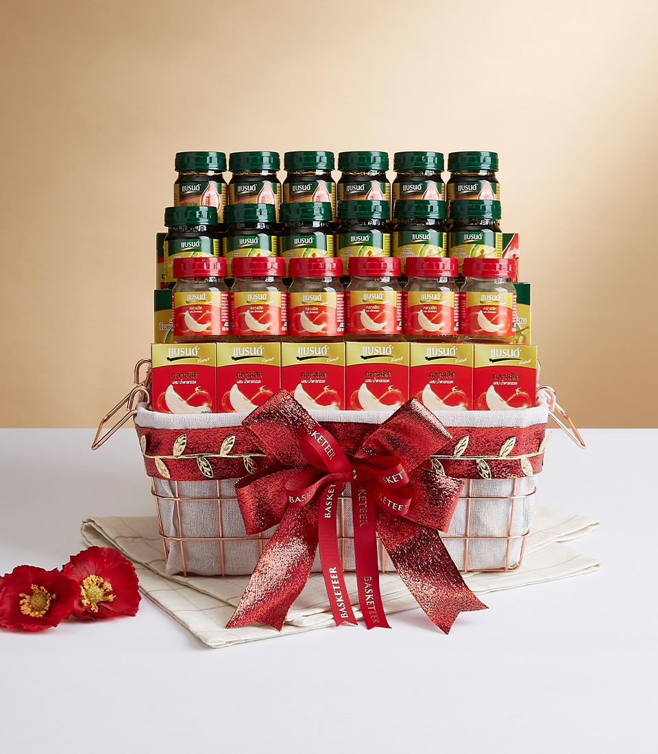 A luxurious Basketeer gift basket graced with an elegant red bow sits majestically on a pristine white surface, set against a sophisticated beige backdrop. Brimming with an exquisite selection of premium bird's nest beverages in diverse, tantalizing flavors, this opulent basket is the epitome of indulgence. Beside it, two vibrant red flowers complement the scene, accompanied by a meticulously folded white napkin. A true hallmark of elegance and refined taste.