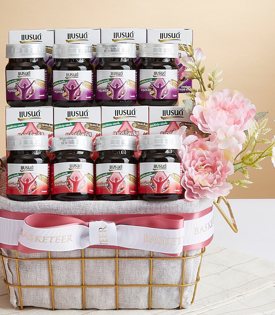 An exquisite gift basket by Basketeer, showcasing twelve elegantly curated jars of Jiusua brand products, meticulously arranged in a sophisticated grid. This luxurious ensemble is adorned with delicate pink and white artificial flowers and a sumptuous white ribbon embellished with opulent gold lettering. The scene is set against a chic beige and white backdrop, radiating elegance and inviting indulgence.