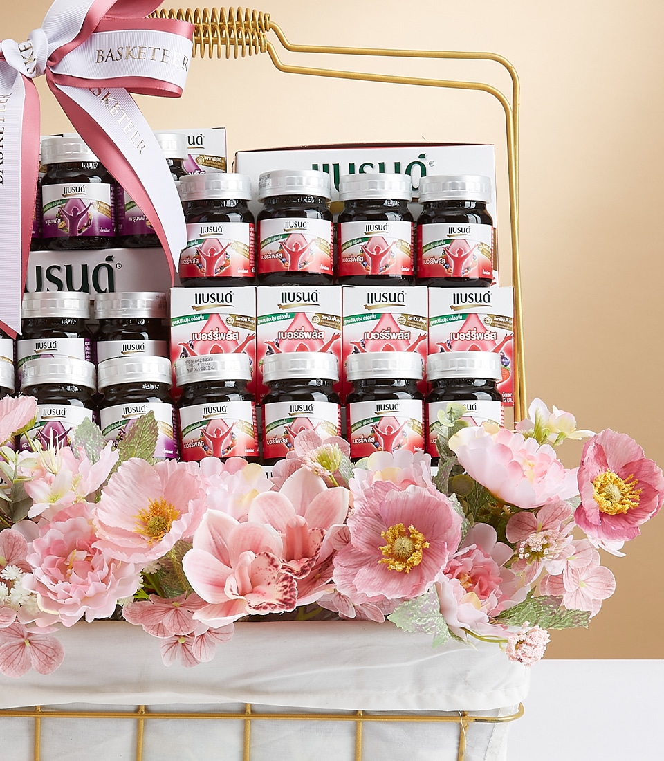 A luxurious gift basket from Basketeer, elegantly adorned with a signature ribbon showcasing the brand’s logo. This exquisite offering features an array of meticulously arranged jars and boxes brimming with premium herbal and fruit extracts. Delicately accented with pastel pink flowers, the opulent presentation is both enchanting and inviting against the chic simplicity of a beige backdrop.