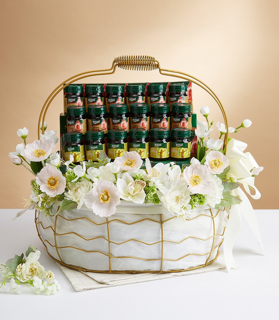 A luxurious, hand-curated gift basket radiating sophistication and charm, filled with an assortment of premium green-labeled sauces. The exquisite basket, a Basketeer masterpiece, is adorned with delicate white and pale pink flowers, enhancing its elegance. A finely crafted gold handle gracefully arches over the arrangement, while a soft white cloth lines the bottom to provide a pristine backdrop for the products. Look for the Basketeer logo that signifies unparalleled quality and indulgence in gifting.