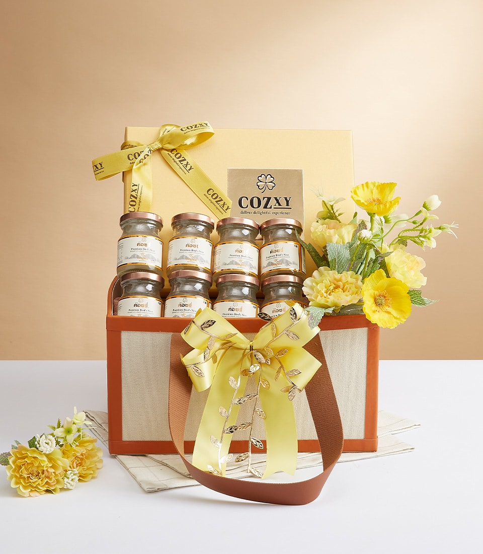 Luxurious gift basket featuring an exquisite collection of Cozzy honey jars, elegantly adorned with vibrant yellow ribbons. The arrangement is enhanced by a stunning assortment of delicate yellow flowers and lush green foliage, creating an inviting and delightful presentation. The beige and brown color palette of the basket exudes sophistication, while subtle touches like the Basketeer logo on a ribbon add a hint of exclusivity. This serene scene is beautifully set against a soft beige background, making it perfect for gifting or indulgence.