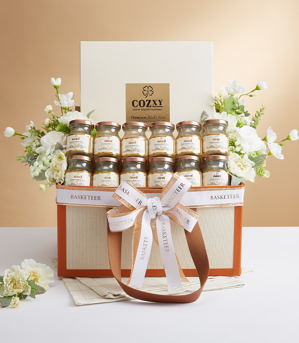 กระเช้าของขวัญทรงสี่เหลี่ยมผืนผ้าหรูหรานำเสนอ Cozy Premium Bird's Nest จำนวน 12 กระปุก จัดเรียงอย่างพิถีพิถันเป็นสามแถวอย่างประณีต ตะกร้าประดับอย่างหรูหราด้วยดอกไม้สีขาวบริสุทธิ์และริบบิ้นสีขาวและน้ำตาลอันประณีตที่แสดงถึงความภาคภูมิ 