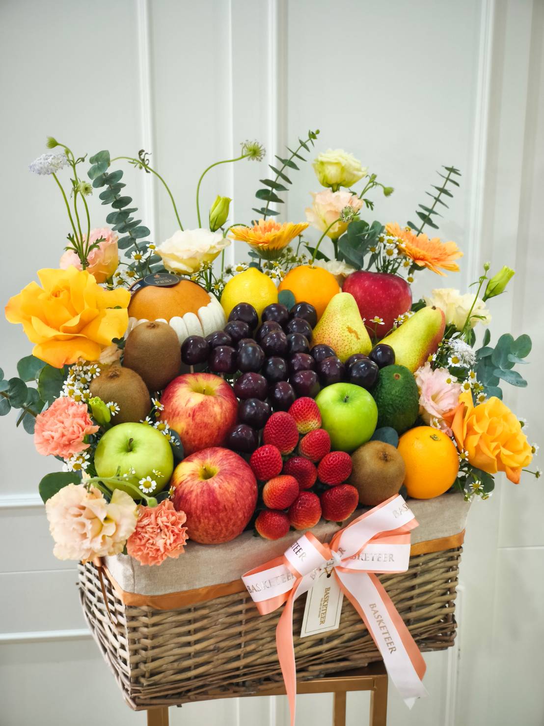 Luxury fruit basket with red and green apples, grapes, strawberries, kiwi, pear, citrus, and yellow roses, accented with fresh flowers and eucalyptus.