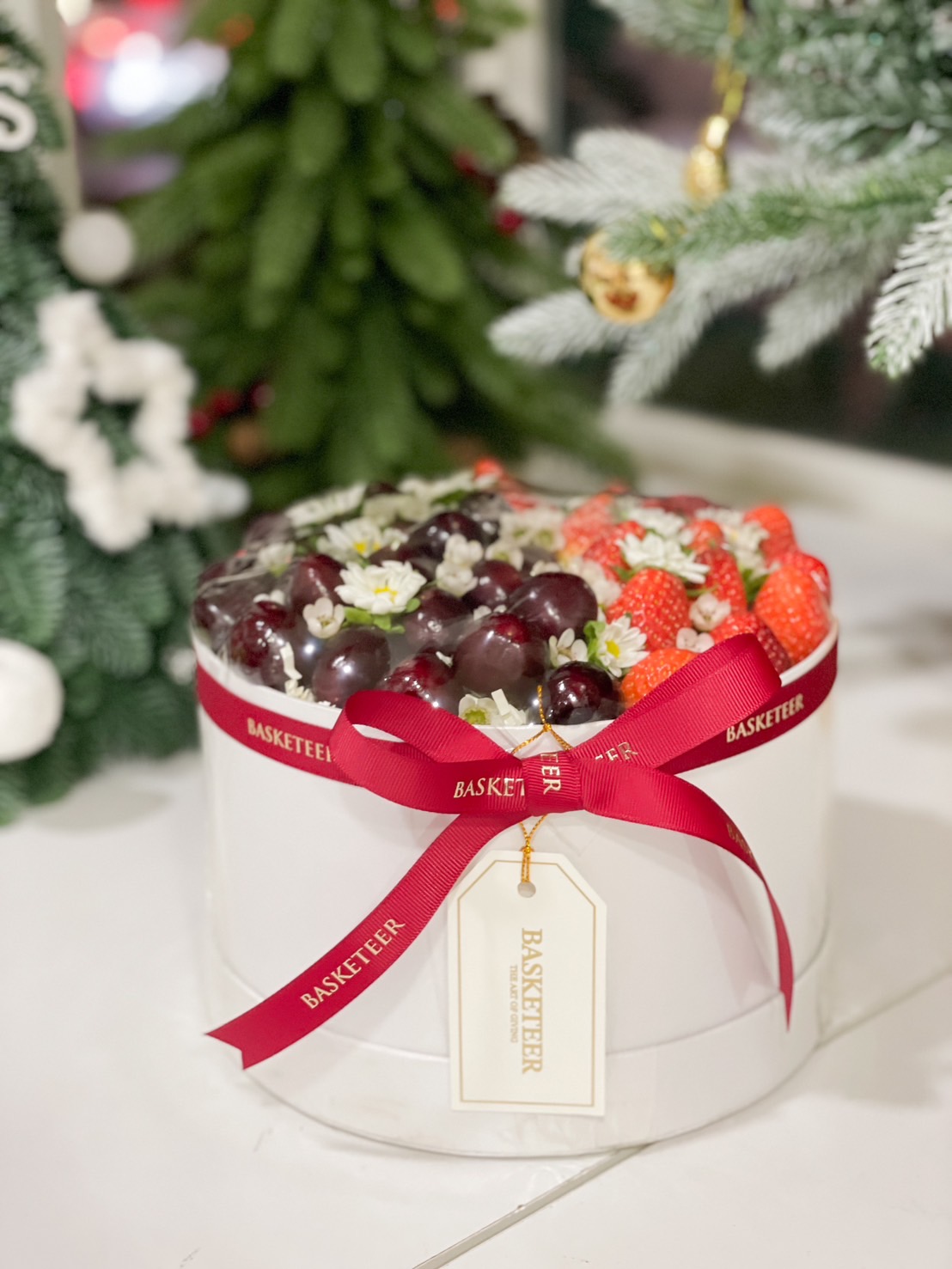 Round gift box with fresh strawberries, cherries, and delicate floral decorations by Basketeer.