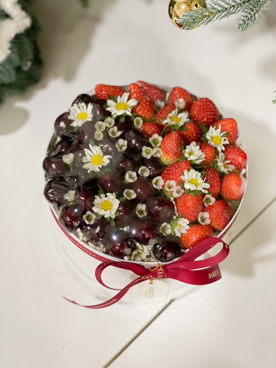 Round gift box with fresh strawberries, cherries, and delicate floral decorations by Basketeer.