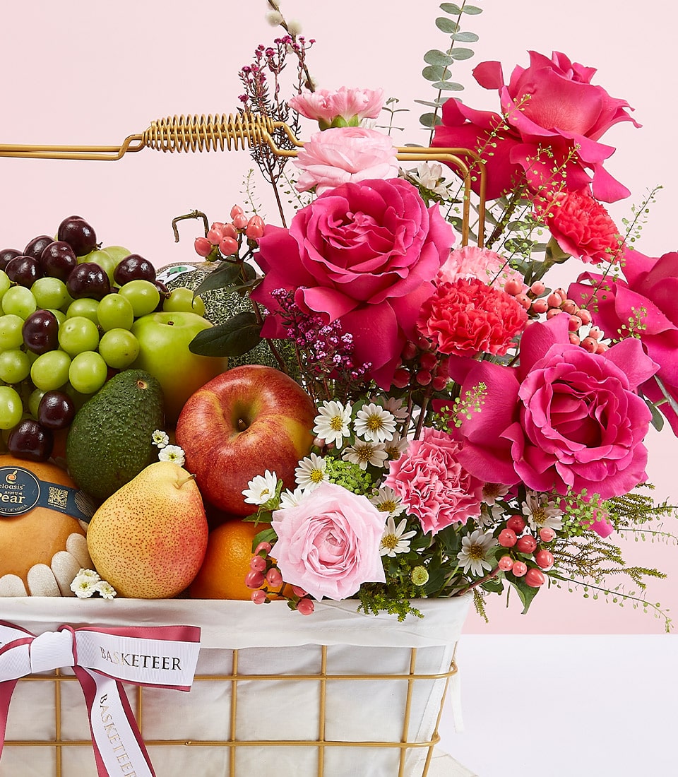 The opulent Fruit Rose Delight Basket by Basketeer offers a splendid array of fresh, premium fruits such as luscious grapes, crisp apples, creamy avocados, and succulent pears. These exquisite selections are elegantly nestled among a breathtaking ensemble of vibrant pink and red roses, delicate carnations, and cheerful daisies. The basket is exquisitely finished with a pristine white bow that proudly displays the distinguished 