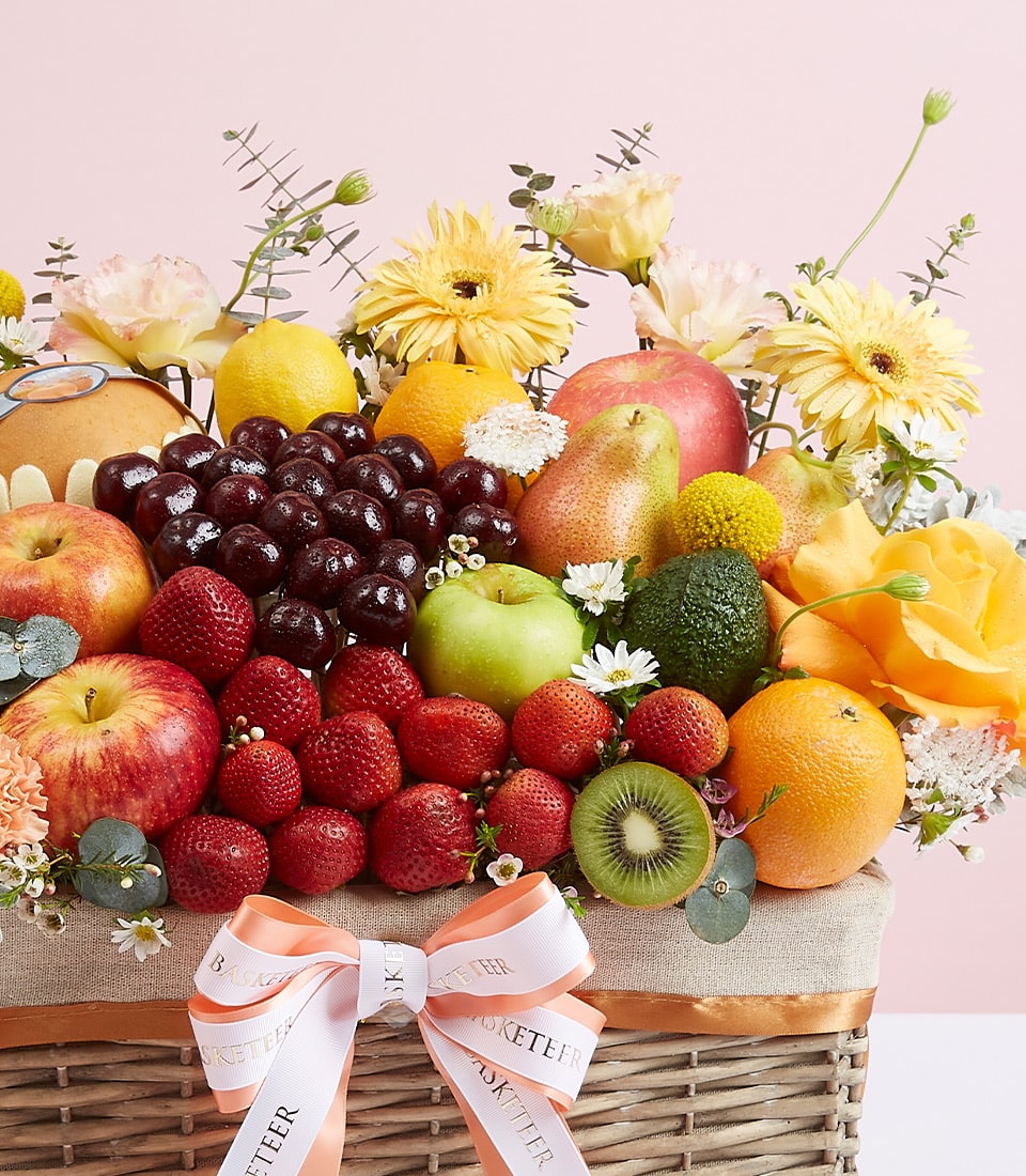 A luxurious wicker basket, brimming with a curated selection of the freshest fruits: crisp apples, plump grapes, succulent strawberries, delectable pears, vibrant kiwis, and zesty oranges. The arrangement is exquisitely adorned with delicate yellow and white flowers. Completing this elegant presentation is a pristine white ribbon elegantly tied into a bow, proudly displaying the 