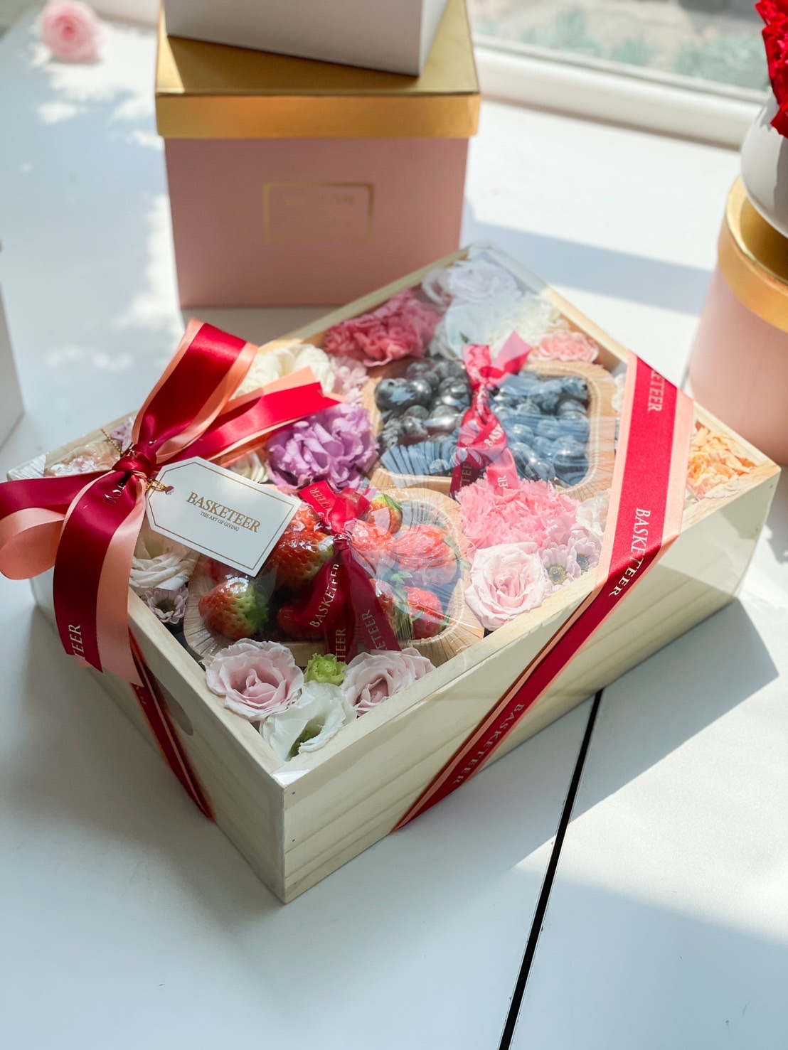A luxurious fruit gift hamper featuring strawberries, fresh berries, and elegant florals in a wooden box, wrapped with a red ribbon for a romantic touch.