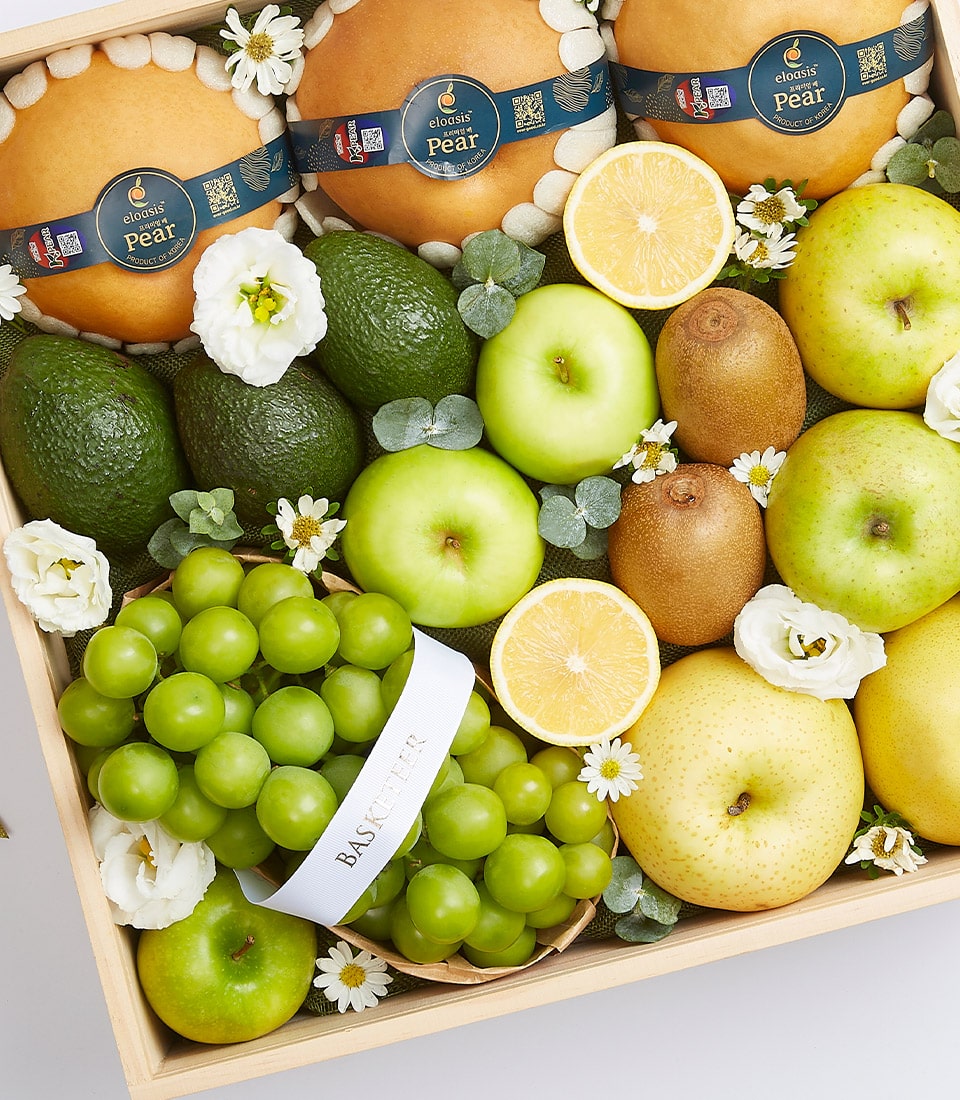 An extravagant fresh fruit crate overflowing with nature's finest offerings: luscious green grapes, golden-hued pears, crisp green apples, succulent kiwi fruits, creamy avocados, and a vibrant half-sliced orange. Delicate decorative white flowers are artistically scattered throughout for an added touch of elegance. Nestled among the grapes is a pristine white ribbon adorned with the sophisticated 