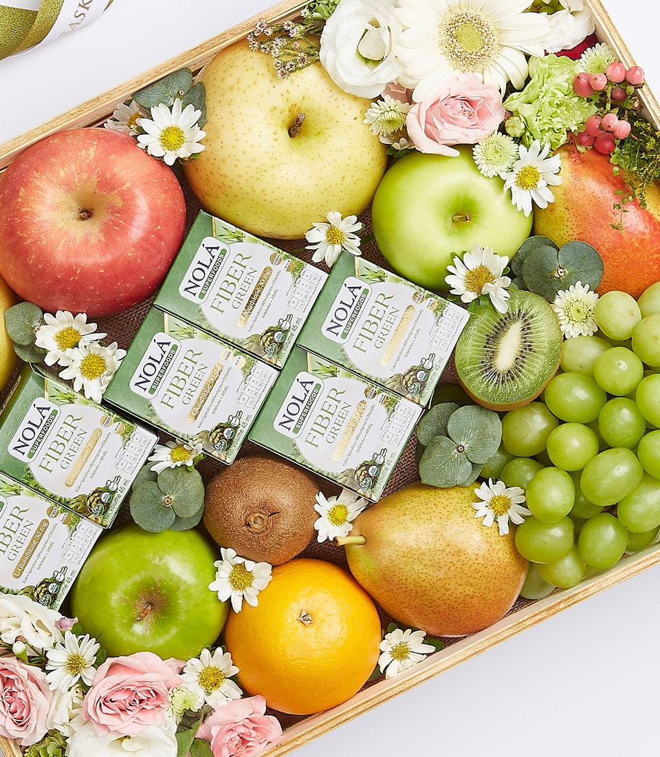 A lavish wooden tray brimming with an assortment of premium fresh fruits, including crisp apples, succulent grapes, juicy pears, vibrant oranges, and exotic kiwis, all nestled amongst delicate floral decorations. This elegant ensemble features several sophisticated boxes of Nola Fiber Chews thoughtfully arranged amidst the fruits and blossoms. The scene is completed with an opulent touch by a ribbon elegantly tied with the Basketeer logo, making this Fresh Fruit Fiber Gift Box a true embodiment of luxury and indulgence.