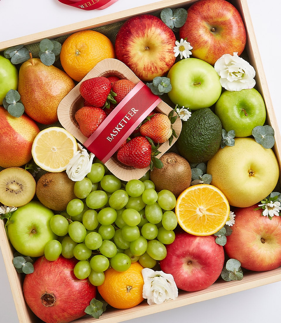 An opulent display of hand-selected fruits elegantly nestled in a handcrafted wooden box. This curated assortment includes crisp apples, succulent pears, vibrant oranges, exotic kiwis, creamy avocados, luscious strawberries, juicy grapes, and a zesty lemon half. Each fruit is exquisitely adorned with delicate white flowers and verdant leaves. At the heart of this lavish presentation is a striking red ribbon emblazoned with the prestigious 