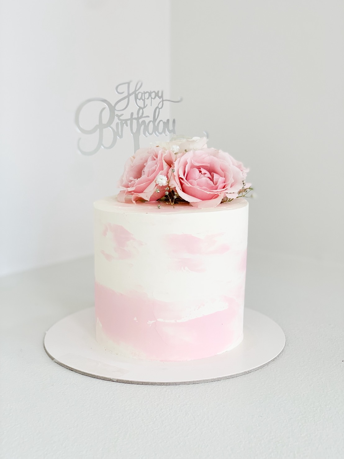 Pastel pink and white buttercream cake topped with fresh pink roses and 