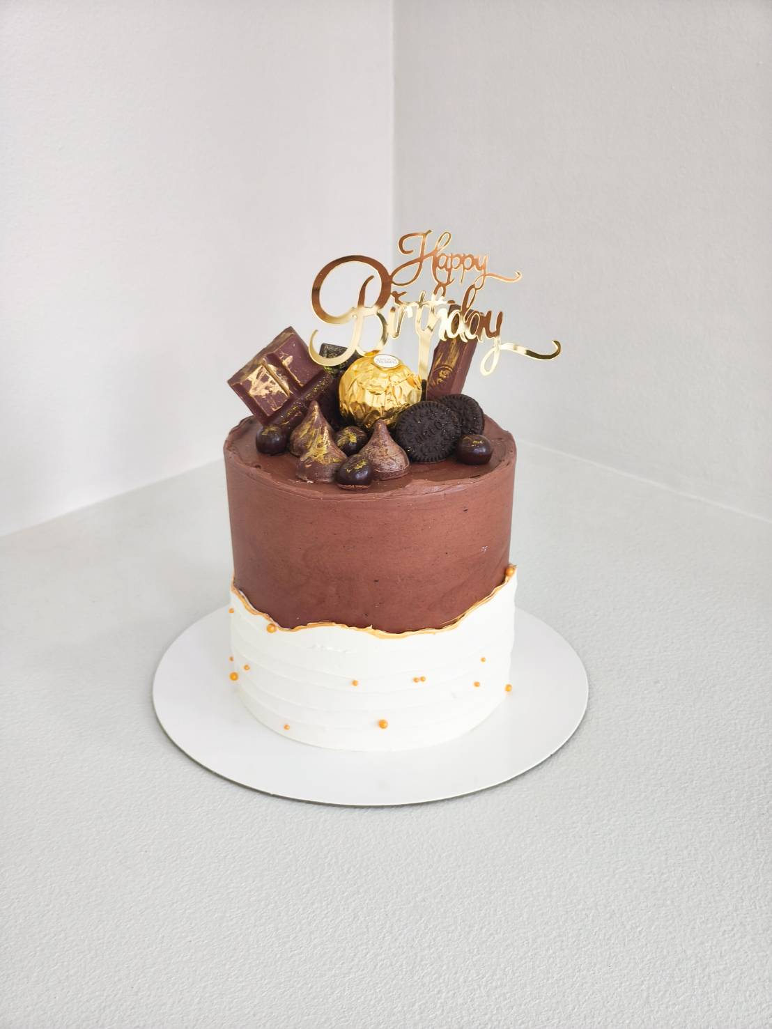 Luxury chocolate birthday cake topped with Ferrero Rocher, Hershey’s, Oreos, and premium chocolates, finished with golden Happy Birthday topper.