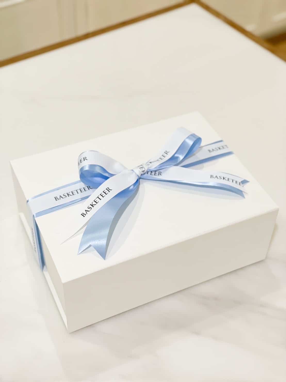 A white rectangular gift box is tied with a light blue ribbon that has the word 