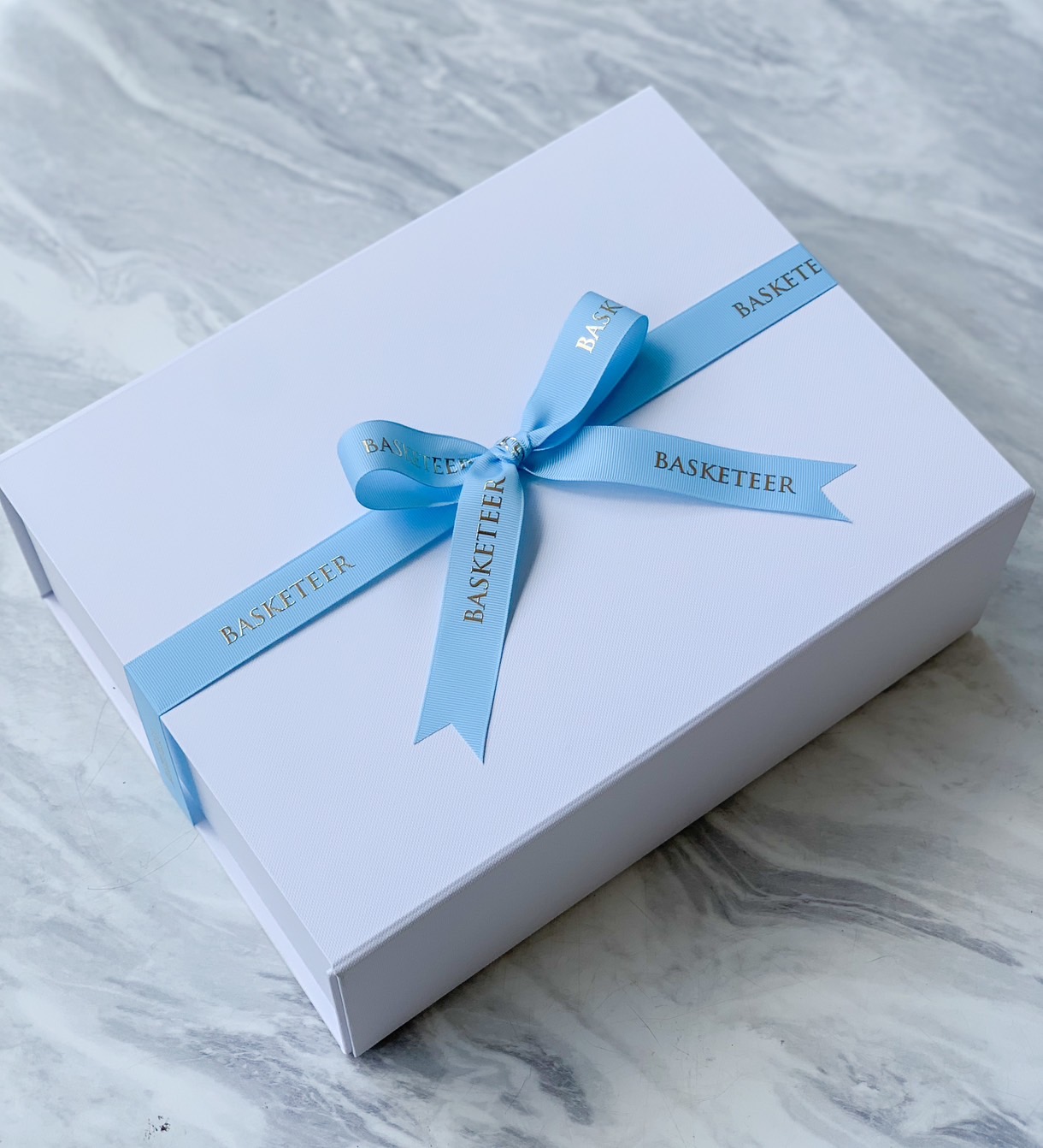 A white gift box is adorned with a light blue ribbon printed with the word 