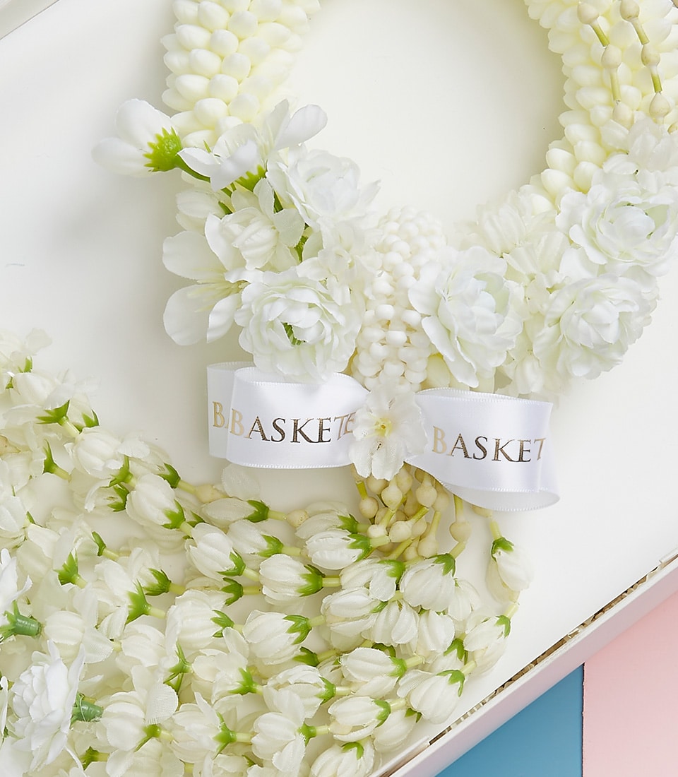 An exquisite white floral garland, adorned with delicate blossoms and lush green accents, is gracefully arranged on a pristine white surface. A luxurious ribbon bearing the elegant gold letters 