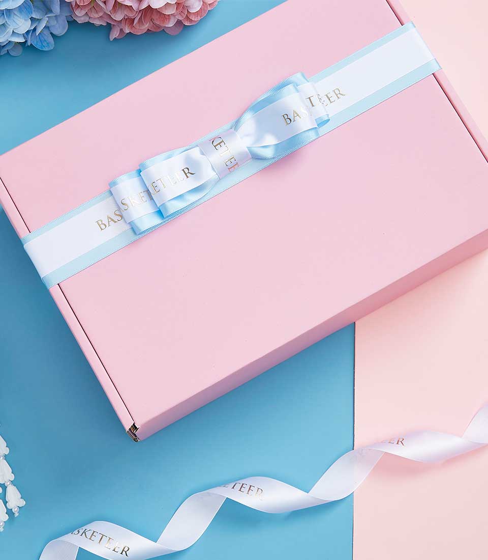An exquisite pink gift box elegantly adorned with a light blue ribbon, beautifully tied in a luxurious bow. The ribbon, branded with the prestigious 