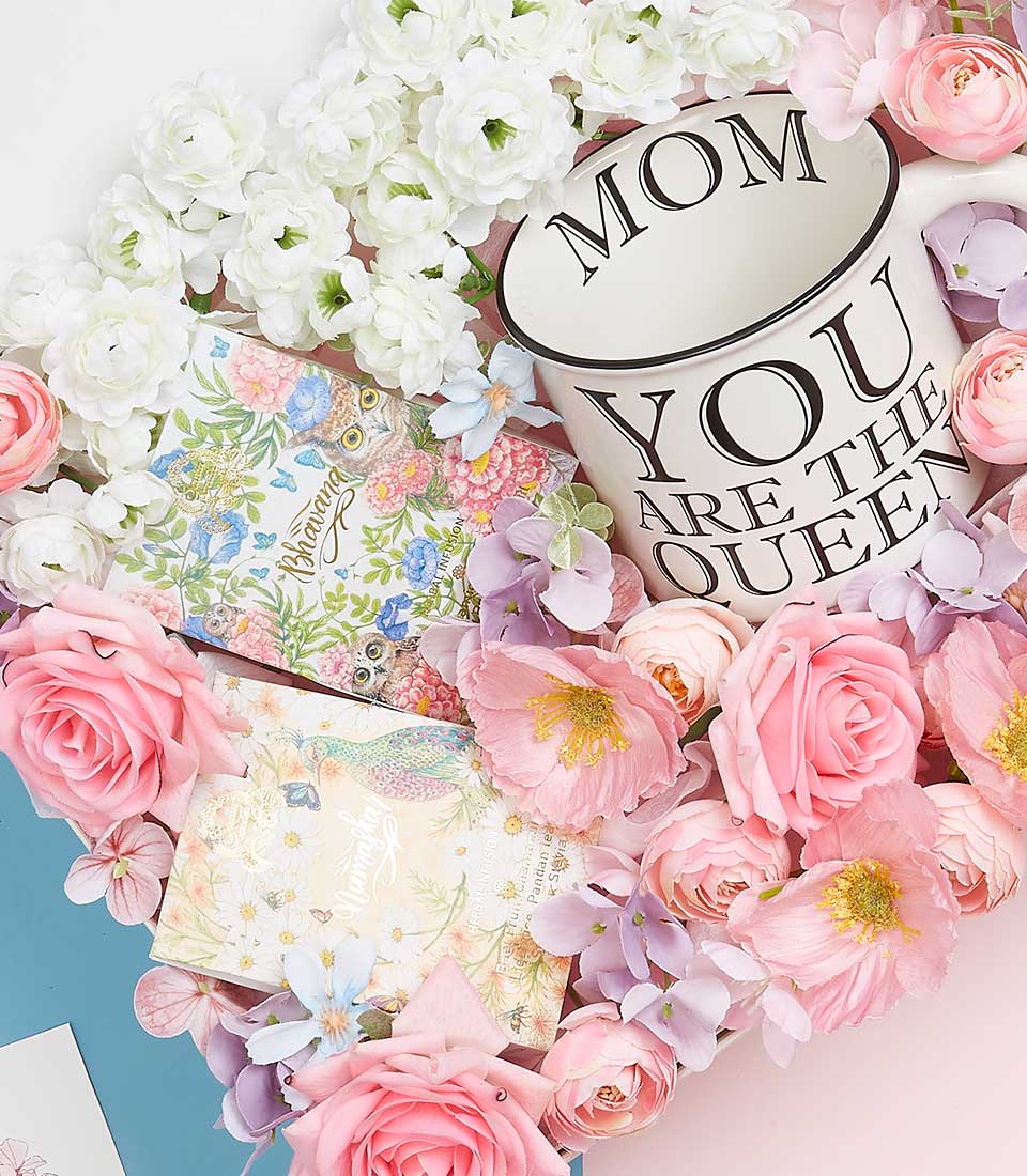 An opulent close-up of a Basketeer Mother's Day gift arrangement, spotlighting an elegant white mug adorned with the statement 