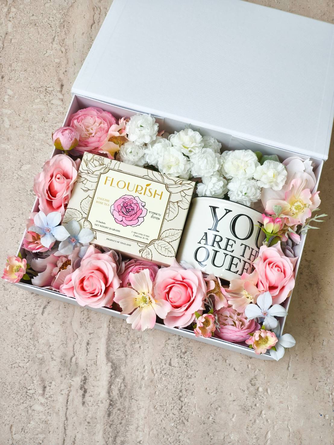 White gift box with English rose tea, “You Are The Queen” mug, and pastel flowers including pink roses and white blossoms.