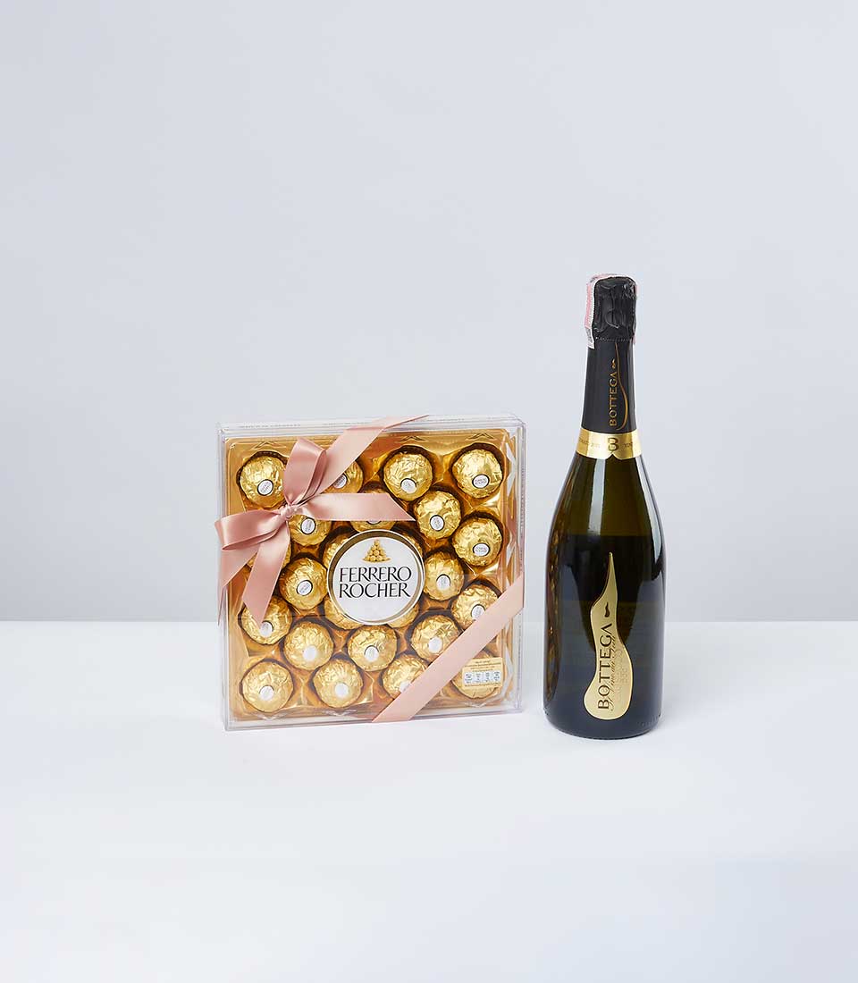 A beautifully curated gift set featuring a box of Ferrero Rocher chocolates, elegantly adorned with a pink ribbon bearing the Basketeer logo, lies enticingly next to an exquisite bottle of Bottega sparkling wine. The luxurious presentation, set against a soft light grey background, invites indulgence and celebration.
