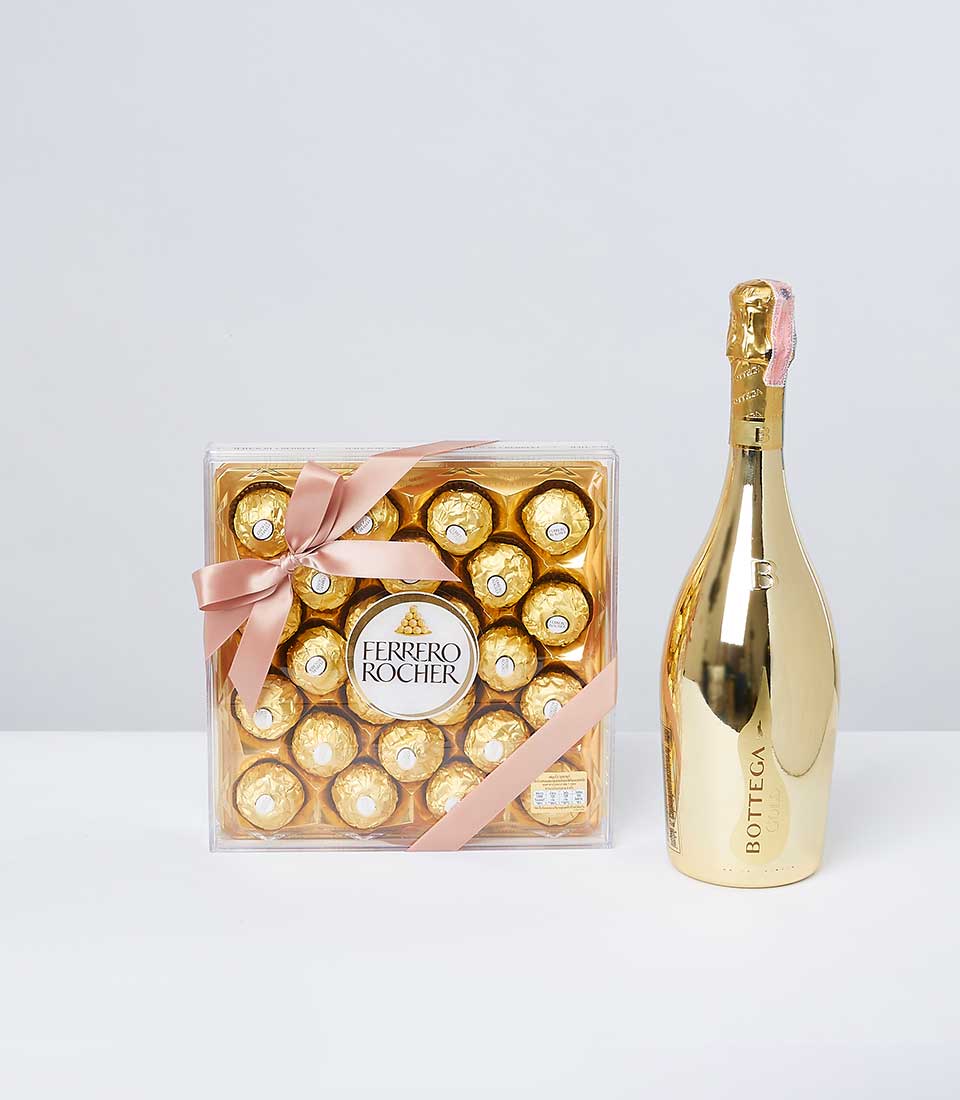 A luxurious gift set elegantly presented: a box of decadent Ferrero Rocher chocolates adorned with a delicate pink ribbon featuring the Basketeer logo, accompanied by a gleaming bottle of Bottega sparkling wine with its opulent gold finish. All set against a pristine white surface, this ensemble evokes indulgence and refinement.