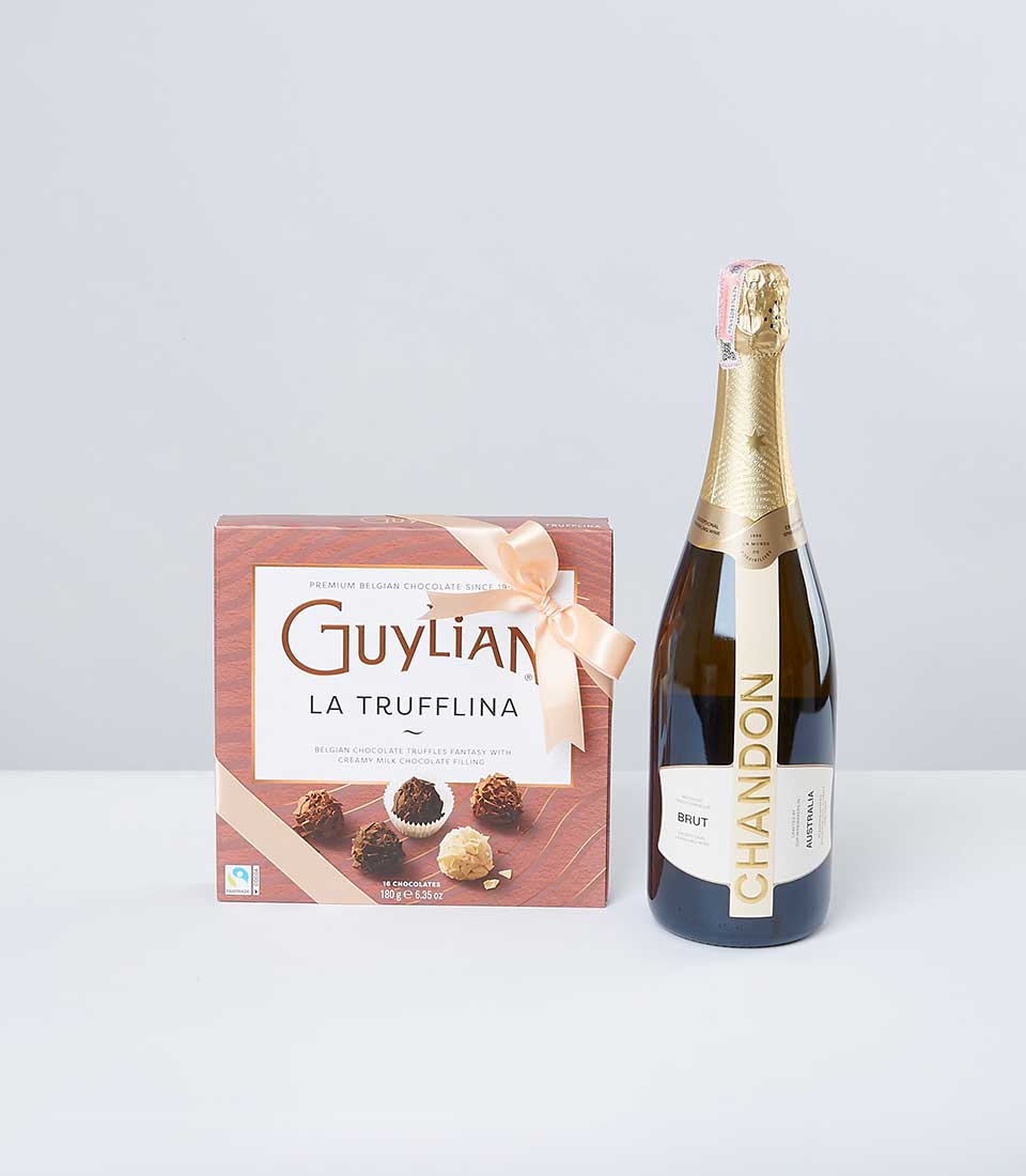 A chic box of Guylian La Trufflina Belgian chocolates, adorned with an elegant ribbon featuring the Basketeer logo, sits gracefully next to an exquisite bottle of Chandon Brut sparkling wine. The luxurious pair is beautifully showcased against a minimalist gray backdrop, inviting indulgence and sophistication.