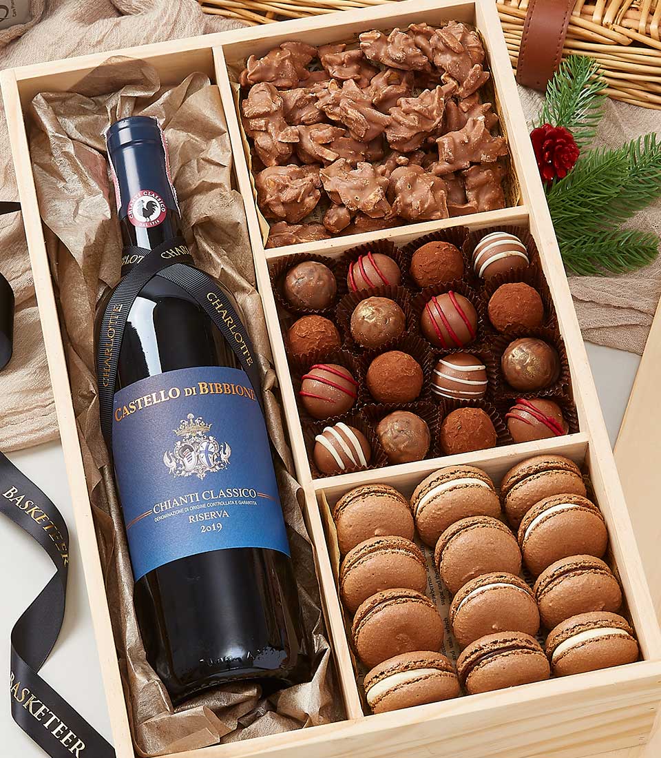 A beautifully crafted wooden gift box adorned with the elegant Basketeer logo cradles a bottle of premium Castello di Bibbione Chianti Classico wine. Nestled alongside are decadent assorted chocolates, exquisite pralines, and luxurious brown macarons. The enchanting scene is further elevated by a backdrop of a rustic wicker basket and sophisticated festive decorations featuring lush pine branches and a vibrant red ribbon.