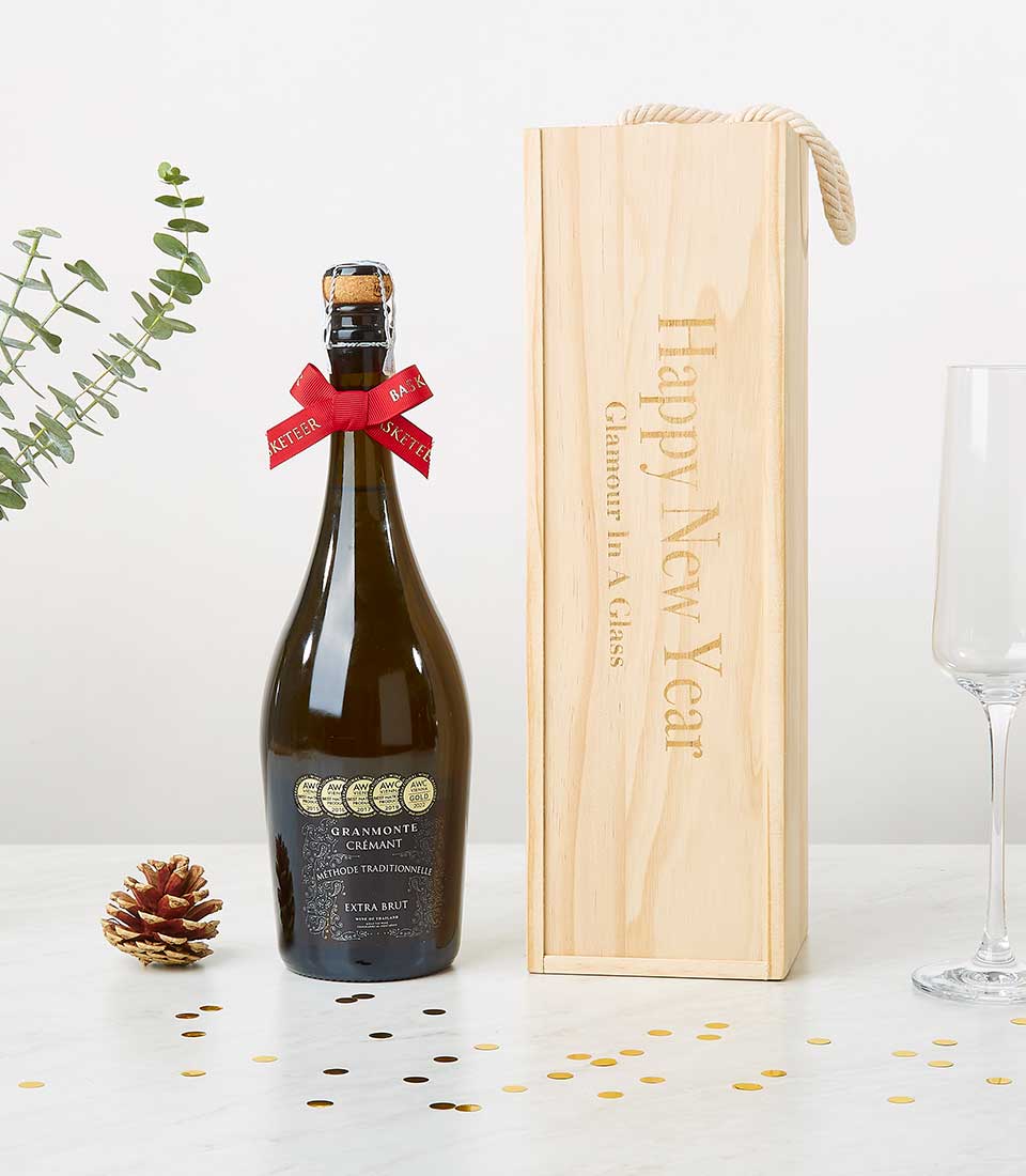 A bottle of luxurious sparkling wine, elegantly adorned with a red ribbon featuring the Basketeer logo, graces the scene. It is complemented by a finely crafted wooden box with 