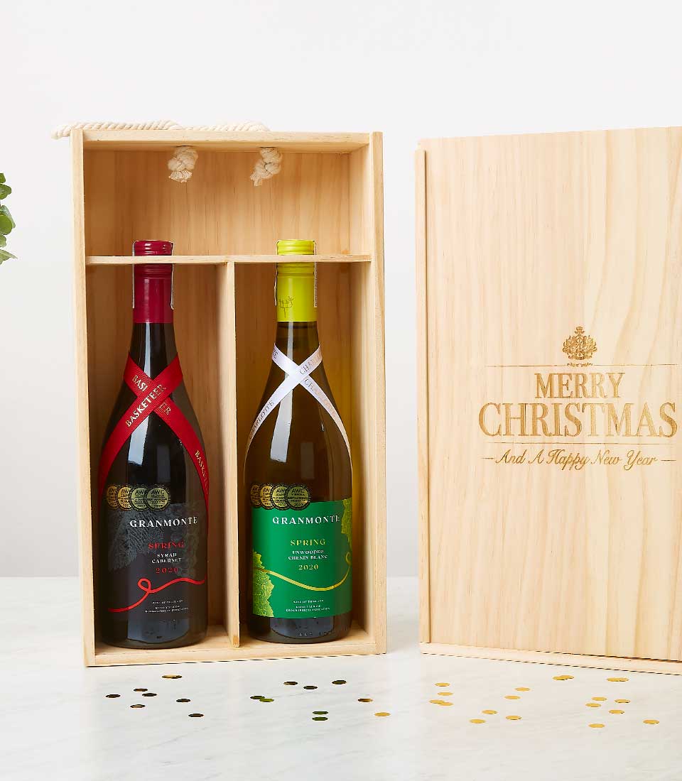 A luxurious wooden box from Basketeer, adorned with elegant branding, rests gracefully on a pristine white surface. Within the box, two exquisite bottles of GranMonte wine—one red and one white—beckon invitingly. The propped-open lid showcases an artful 