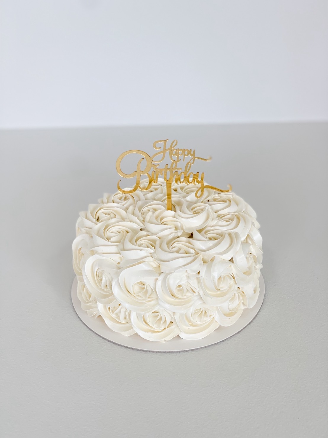 Elegant white rosette buttercream birthday cake with gold Happy Birthday topper for celebrations and luxury gifting.
