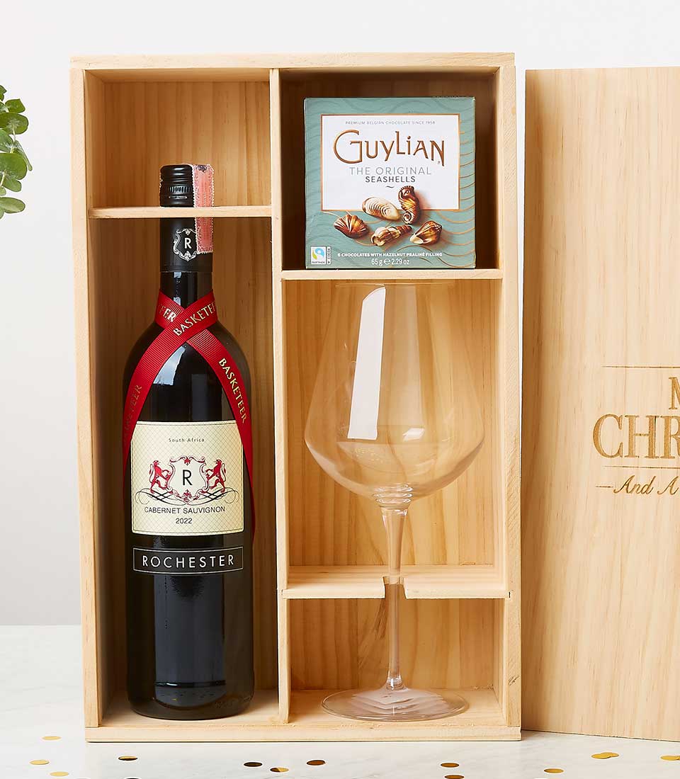 Luxurious Basketeer wooden gift box showcased on an elegant white surface. Inside, you'll find a distinguished bottle of Rochester Cabernet Sauvignon wine, complemented by a beautifully crafted wine glass, and a delectable box of Guylian Belgian chocolate seahorses. Each item is perfectly nestled in its own compartment for an opulent presentation. The partially visible lid features the sophisticated Basketeer logo, adding an extra touch of exclusivity to this exquisite ensemble.