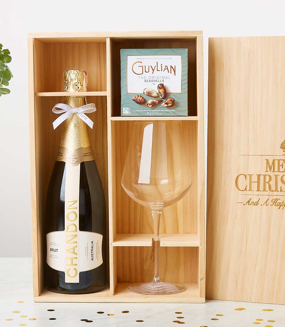 An elegant wooden gift box from Basketeer beautifully showcases a bottle of Chandon Brut champagne, a generously sized wine glass, and an exquisite box of Guylian chocolate seashells. The lid, adorned with the festive inscription 