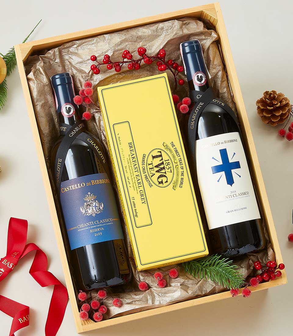 An opulent Basketeer gift box featuring two exquisite bottles of Chianti Classico wine, accompanied by a luxurious yellow box of gourmet cookies. The wines are elegantly nestled amidst festive holiday adornments, including vibrant red berries, rustic pine cones, and lush green sprigs. A sophisticated red ribbon gracefully adorned with the letters 