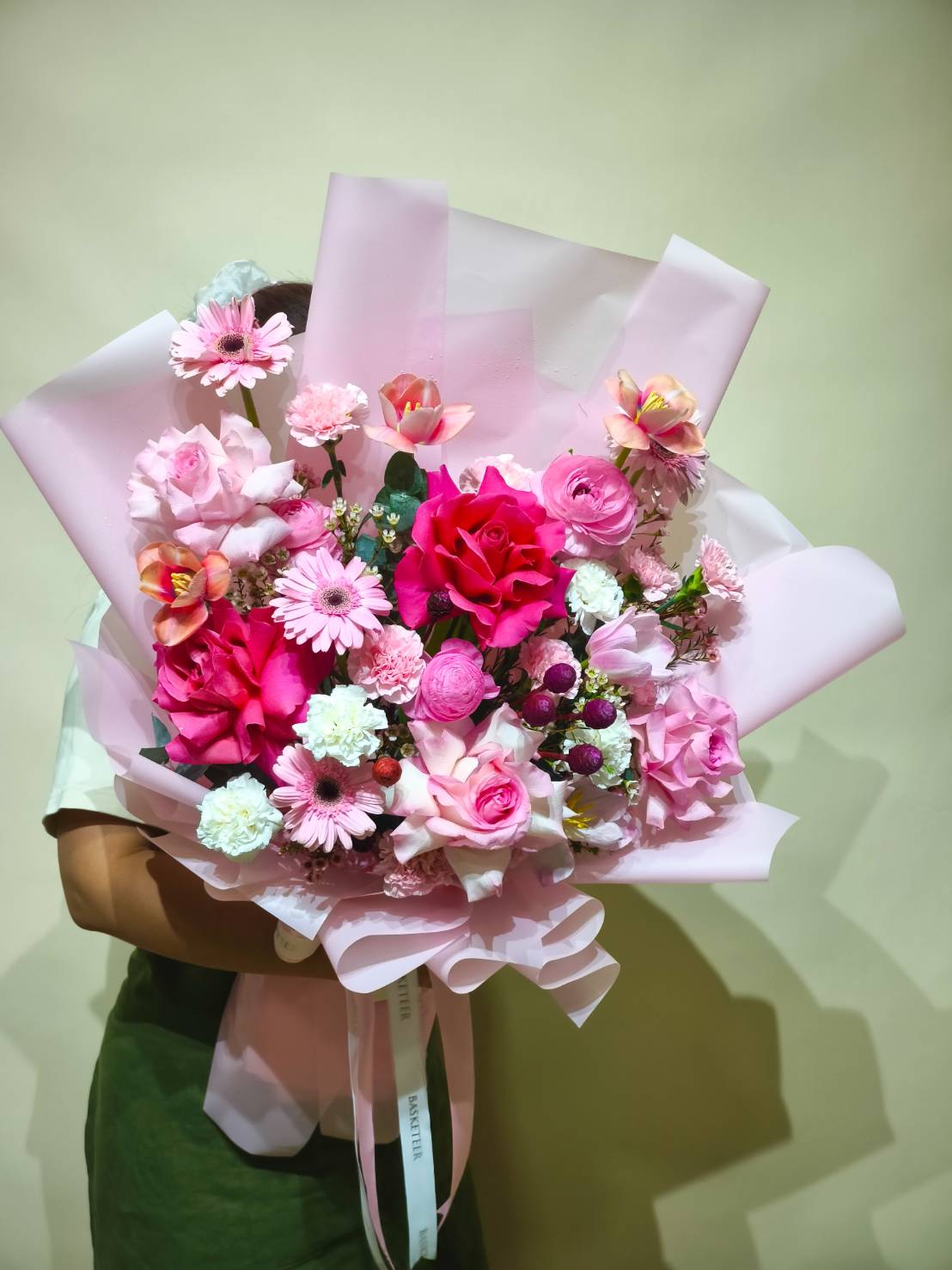 Bouquet of vibrant pink roses, gerberas, ranunculus, carnations, and mixed blooms wrapped in pink paper.