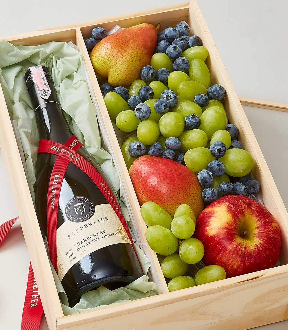 A luxurious wooden gift box from Basketeer, proudly showcasing an elegant array of delights. The left compartment cradles a prestigious bottle of Pepperjack wine, exquisitely wrapped in lush green tissue paper and adorned with a rich red ribbon, complete with the Basketeer logo. To the right, a bountiful selection of the Finest green grapes, plump blueberries, crisp pears, and vibrant apples await to offer unparalleled freshness and indulgence.