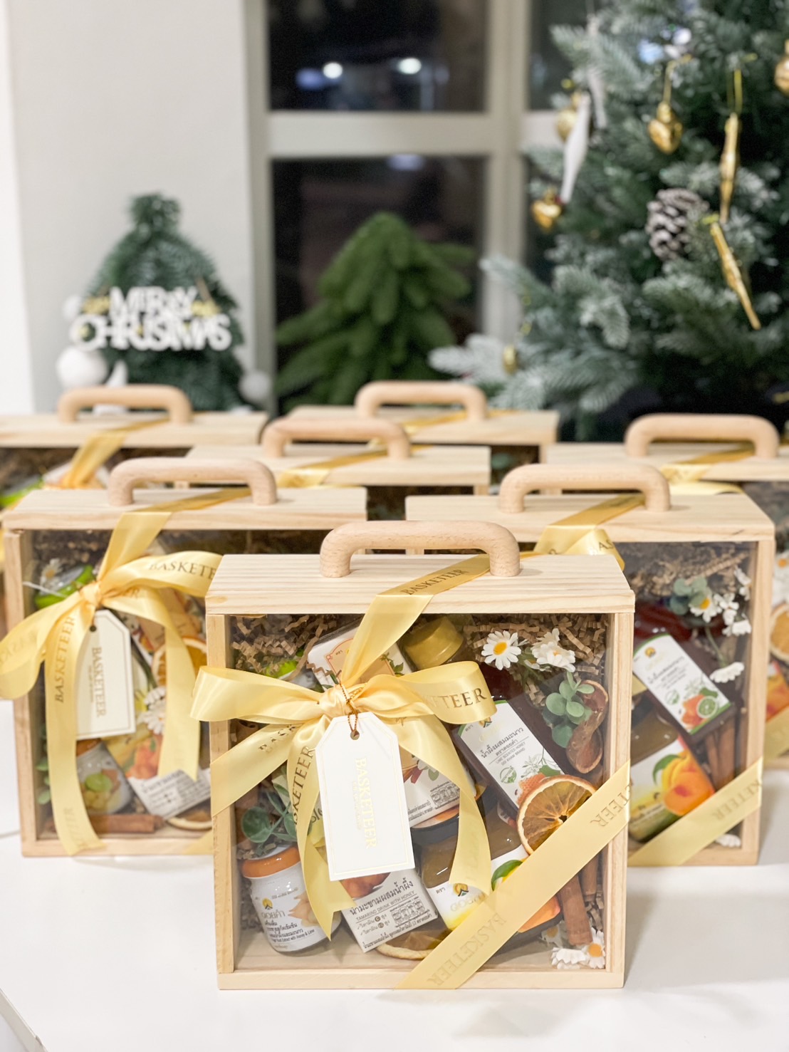 Natural Wellness Gift Set in a wooden box with a clear lid, featuring herbal drinks, honey, and wellness products, tied with a yellow ribbon.