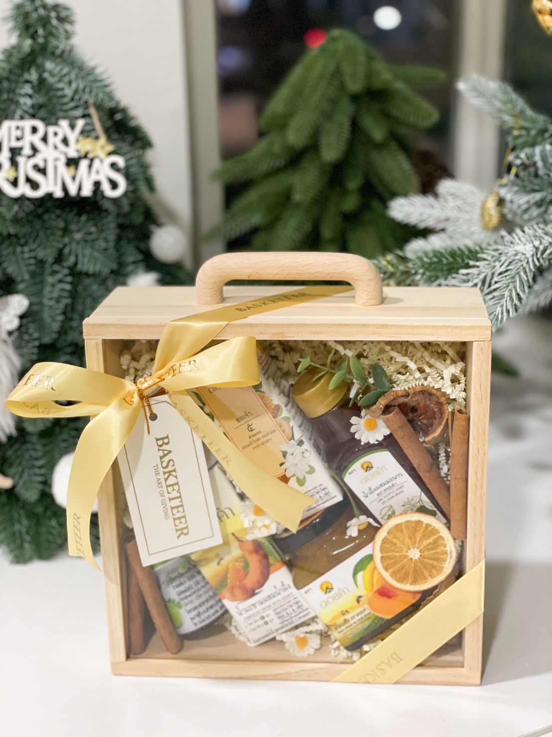 Natural Wellness Gift Set in a wooden box with a clear lid, featuring herbal drinks, honey, and wellness products, tied with a yellow ribbon.